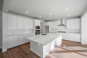 Kitchen featuring white cabinetry, sink, oven, and wall chimney range hood