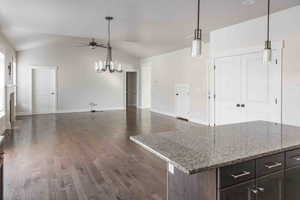 Kitchen with ceiling fan with notable chandelier, light stone countertops, dark wood-type flooring, and vaulted ceiling