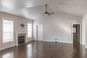 Unfurnished living room with a textured ceiling, dark hardwood / wood-style flooring, a fireplace, and vaulted ceiling