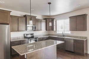 Kitchen with dark wood-type flooring, sink, decorative light fixtures, light stone counters, and stainless steel appliances