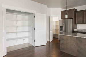 Kitchen with light stone countertops, stainless steel fridge, dark brown cabinetry, dark wood-type flooring, and hanging light fixtures