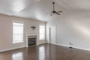 Unfurnished living room with a stone fireplace, ceiling fan, dark wood-type flooring, and vaulted ceiling