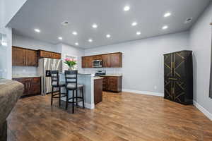 Kitchen featuring a center island, darkLVP flooring, a kitchen bar, dark brown cabinets, and appliances with stainless steel finishes