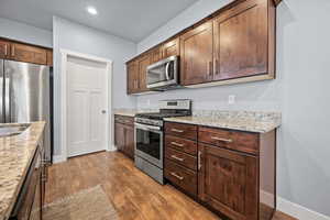 Kitchen with light stone countertops, dark brown cabinetry, stainless steel appliances, and dark LVP flooring