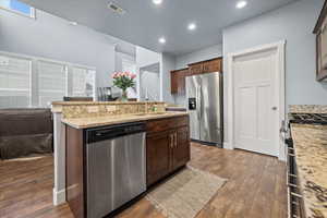 Kitchen with dark LVP flooring, dark brown cabinetry, light stone counters, and appliances with stainless steel finishes