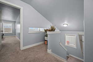 Hallway featuring light colored carpet, lofted ceiling, and a textured ceiling