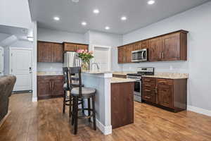 Kitchen with light granite countertops, stainless steel appliances, dark LVP flooring, and a center island with sink