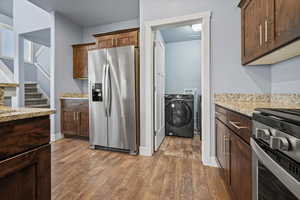 Kitchen with washing machine and clothes dryer, light stone counters, dark LVP flooring, and stainless steel appliances