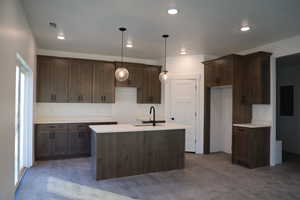 Kitchen with dark brown cabinets, a kitchen island with sink, dark wood-type flooring, sink, and pendant lighting