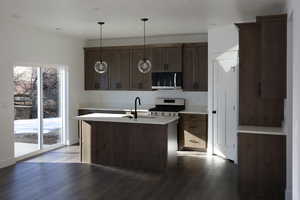 Kitchen with a kitchen island with sink, sink, dark floors, appliances with stainless steel finishes, and decorative light fixtures