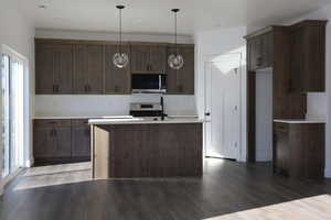 Kitchen with dark wood-style flooring, range oven, pendant light fixtures, and an island with sink