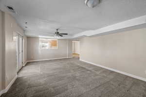 Unfurnished room with carpet flooring, ceiling fan, a raised ceiling, and a textured ceiling