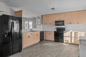 Kitchen featuring a textured ceiling, sink, black appliances, light brown cabinets, and light hardwood / wood-style flooring