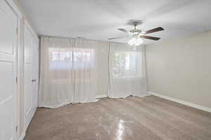 Carpeted spare room with ceiling fan, plenty of natural light, and a textured ceiling