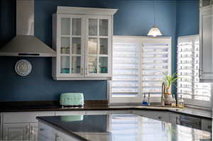 Kitchen featuring wall chimney exhaust hood, cooktop, sink, decorative light fixtures, and white cabinetry