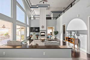 Living room featuring ceiling fan, a multi sided fireplace, a towering ceiling, and dark wood-type flooring