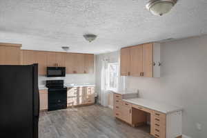 Kitchen with black appliances, a textured ceiling, light brown cabinetry, and light hardwood / wood-style flooring