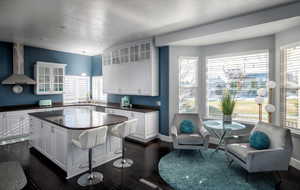 Kitchen with dark wood-type flooring, wall chimney range hood, decorative light fixtures, a center island, and white cabinetry