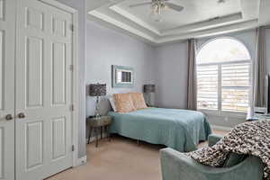 Bedroom with light colored carpet, a raised ceiling, and ceiling fan