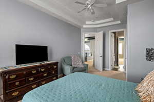 Bedroom with light colored carpet, a raised ceiling, and ceiling fan