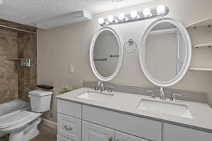 Full bathroom featuring a textured ceiling, vanity, toilet, and tiled shower / bath combo