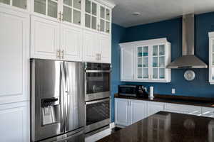 Kitchen with stainless steel appliances, white cabinetry, and wall chimney range hood