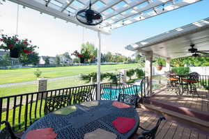 Wooden deck featuring a lawn, ceiling fan, a fenced in pool, and a pergola