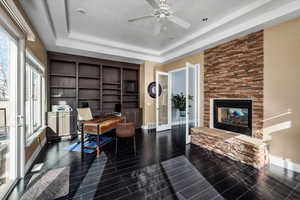 Office area featuring a stone fireplace, a raised ceiling, and dark wood-type flooring