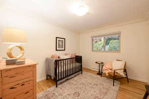 Bedroom with a baseboard heating unit, light hardwood / wood-style flooring, a nursery area, and crown molding