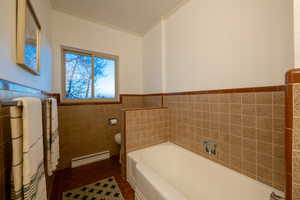 Bathroom featuring toilet, ornamental molding, baseboard heating, and tile walls