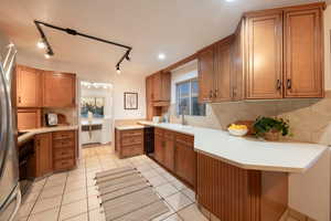 Kitchen with kitchen peninsula, light tile patterned floors, tasteful backsplash, and sink