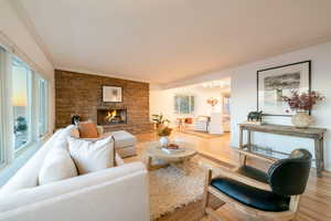 Living room with a stone fireplace, hardwood / wood-style floors, plenty of natural light, and ornamental molding