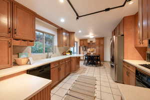 Kitchen with black appliances, decorative backsplash, light tile patterned flooring, and sink