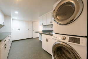 Clothes washing area with sink, cabinets, and stacked washer and clothes dryer