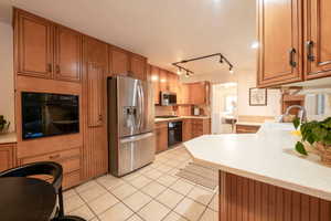 Kitchen with kitchen peninsula, rail lighting, stainless steel appliances, sink, and light tile patterned floors