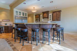 Kitchen featuring stainless steel appliances, an island for food prep, a breakfast bar, custom range hood & granite counters