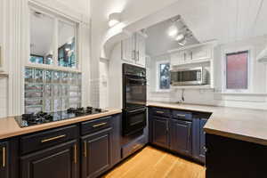 Kitchen featuring decorative backsplash, light wood-type flooring, rail lighting, black appliances, and white cabinets