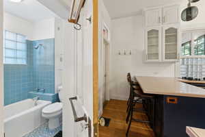 Bathroom featuring backsplash, wood-type flooring, tiled shower / bath combo, and toilet