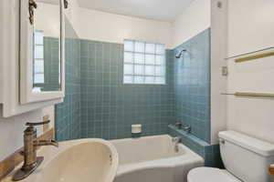 Full bathroom with tiled shower / bath combo, toilet, sink, and natural light