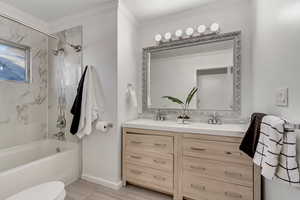 Full bathroom with tiled shower / bath, hardwood / wood-style floors, toilet, vanity, and ornamental molding