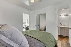 Bedroom with light wood-type flooring, ensuite bathroom, ceiling fan, sink, and a closet