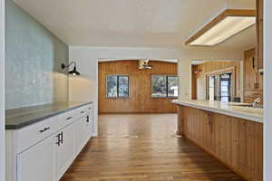 Kitchen with wooden walls, light wood-type flooring, a textured ceiling, white cabinetry, and kitchen peninsula