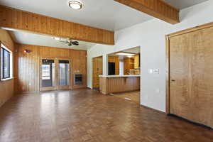 Unfurnished living room with ceiling fan, french doors, dark parquet floors, heating unit, and wooden walls