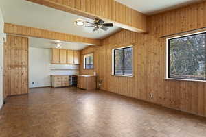 Kitchen with vaulted ceiling with beams, wood walls, light brown cabinetry, and ceiling fan