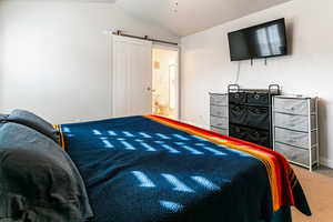 Bedroom featuring carpet flooring, a barn door, ensuite bath, and vaulted ceiling