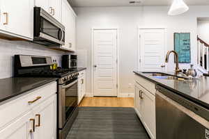 Kitchen featuring white cabinetry, sink, backsplash, appliances with stainless steel finishes, and hardwood / wood-style flooring