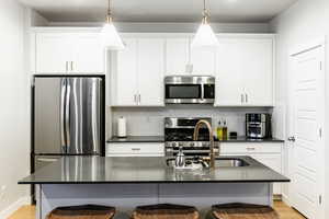 Kitchen with a breakfast bar, a center island with sink, pendant lighting, and appliances with stainless steel finishes