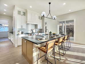 Kitchen with a breakfast bar, a kitchen island with sink, white cabinets, sink, and light hardwood / wood-style flooring