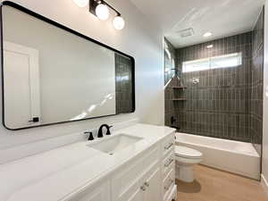 Full bathroom with tiled shower / bath combo, wood-type flooring, a textured ceiling, toilet, and vanity