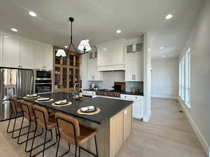 Kitchen featuring white cabinetry, sink, hanging light fixtures, stainless steel appliances, and a kitchen island with sink